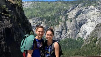A man and woman next to each other smiling in front of a rocky mountain with trees