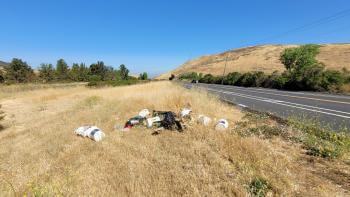 A pile of trash sits on the side of the road among golden grass