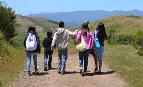 Group of five young adolescents walking away from camera on trail with green hills in distance 