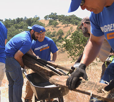 Volunteers in blue Progressive shirts loading fence posts into wheelbarrow
