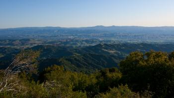 An expansive view looking down and across rows of green and blue mountains stretching to the horizon, with the tops of trees framing the bottom of the photos.