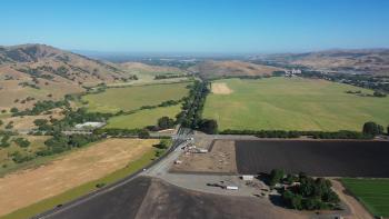 An aerial view of a patchwork of farmlands between two mountain ranges, with a tree-lined road splitting down the middle of the photo.