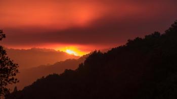 The silhouette of a hillside in the foreground with a orange sky from a fire in the background
