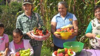 Three adults and two children each hold a basket of fresh produce from a local garden