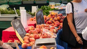 Tables at a farmer's market display fresh produce as an individual walks by
