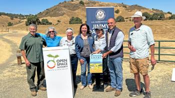 A group of seven adults stand in behind a white podium with the Open Space Authority logo, in front of a partially covered banner that says 'U.S. Representative Jimmy Panetta."