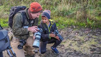 Man and child squatting on the dirt floor smiling and holding cameras