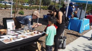 Woman showing a mother and child something at an informational booth with rocks and seeds