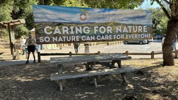 A banner hangs between two trees and says, "Caring for nature so nature can care for everyone"
