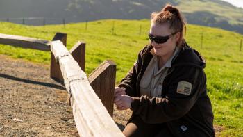 Woman in OSA gear and shades smiling and working on a fence