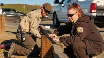 Two OSA staff kneeling down on the dirt ground to work on a low fence