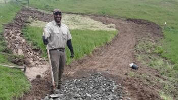 Man holding a tool and standing on a trail path that is under construction