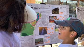 side view of a boy smiling wide in front of a poster board with plans on it
