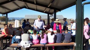 Children sitting down under a gazebo and listening to a man and woman present