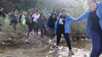 A line of women crossing a lake on stones and holding hands