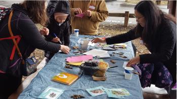 A group of 5 people making crafts at a long table outdoors
