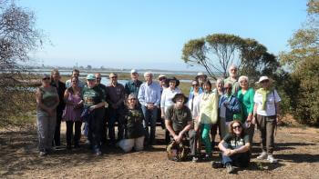 Group of older adults smiling for a photo outside with a blue sky and trees and the background