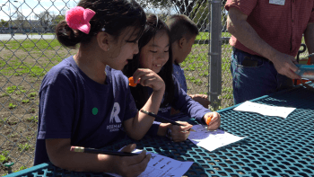 Young students sitting at a table outside and doing a learning activity on paper