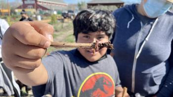 Young boy holding a stick with  a worm on it