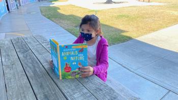 Young girl reading a book at a table outside