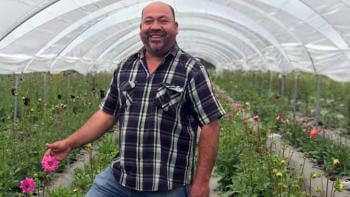A man smiling in a field of flowers under a white tent