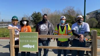 five people standing next to eachother behind Guadalupe River Park fencing
