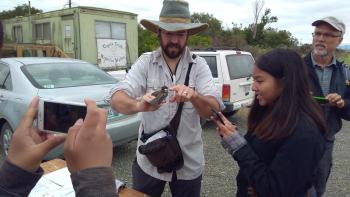 A man holding a small bird and a girl is smiling and taking a photo beside him.