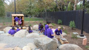 children in purple shirts playing outside in a play area with rocks and mulch