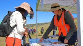 Two people in front of a table looking at a volunteer wearing a hat and an orange vest who is pointing at a map.