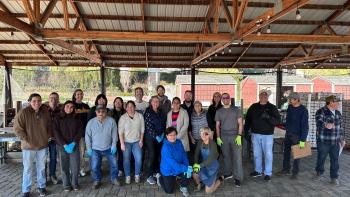 Large group of people standing together and smiling under an overhang outside