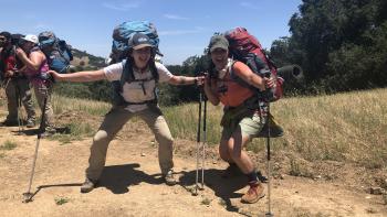 Two women posing with arms out on a trail