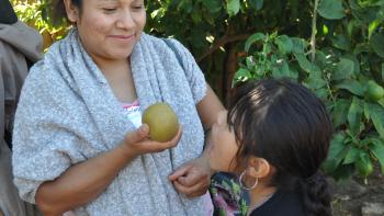 A woman and young girl side by side with a fruit in hand