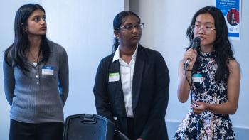 Three young people stand at the front of the room talking to an audience.