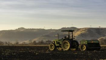 A tractor is parked on agricultural land with grassland hills in the background.