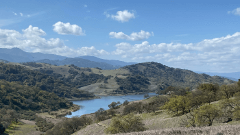 A blue reservoir is surrounded by green and brown hills and mountains
