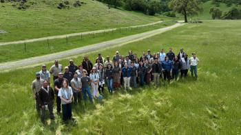 Large group of people standing in green grassy field smiling up at the camera