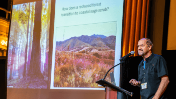 David Ackerly stands at a podium with a screen behind him that reads "How does a redwood forest transition to coastal sage scrub?"