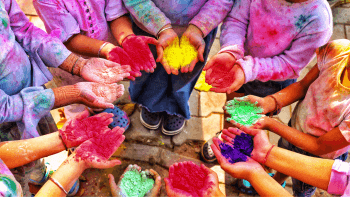 A group of small children stand in a circle with their palms facing up holding powders of different colors