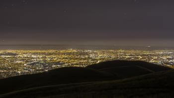A hill overlooks a city lit up with lights at sunset