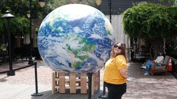 A person stands next to a large inflatable globe in an outdoor space.