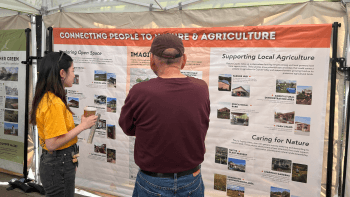 An Open Space Authority staff member and an Earth Day attendee stand in front of a banner for the potential agricultural amenities being considered for Coyote Valley.