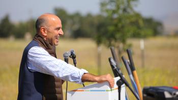 Congressman Jimmy Panetta stands at a podium with a microphone in hand with open space and trees in the background.