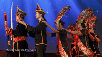 Dusun people of Malaysia stand in a line holding each others shoulders while performing a ritual dance during a harvest festival.