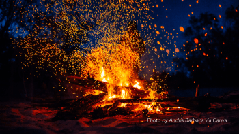 Sparks from a bonfire fly away from the flames and light up the dark blue night sky.