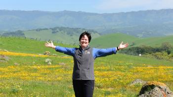 Andrea Mackenzie stands in front of wildflowers at Coyote Ridge with her arms out in celebration