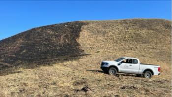 A white truck with the Open Space Authority logo sits next to a golden, grassy hill, part of which has been burned.