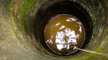 A photo looks down into a well with a bit of murky water at the bottom.