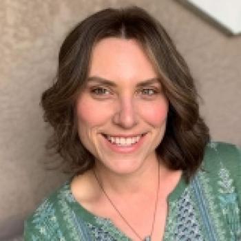 white woman with shoulder length brown hair wearing a green tunic against a tan background