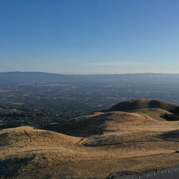 An aerial view of Sierra Vista's rolling gold hillsides with trails winding across them. Beyond the hills is an expansive view of Santa Clara Valley below, under a clear blue sky.