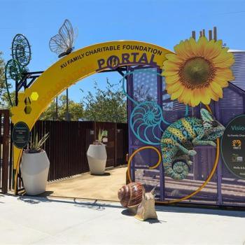 The entrance to an outdoor education area, with a bright yellow arch that reads "Xu Family Charitable Foundation Exploration Portal" surrounded by sculptural and cut-out shapes of a yellow flower, a blue and yellow chameleon, a snail, and a butterfly 